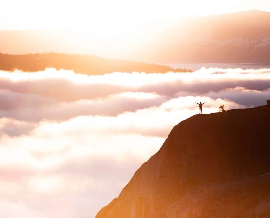 A hiker standing on a mountain summit above the clouds at sunrise