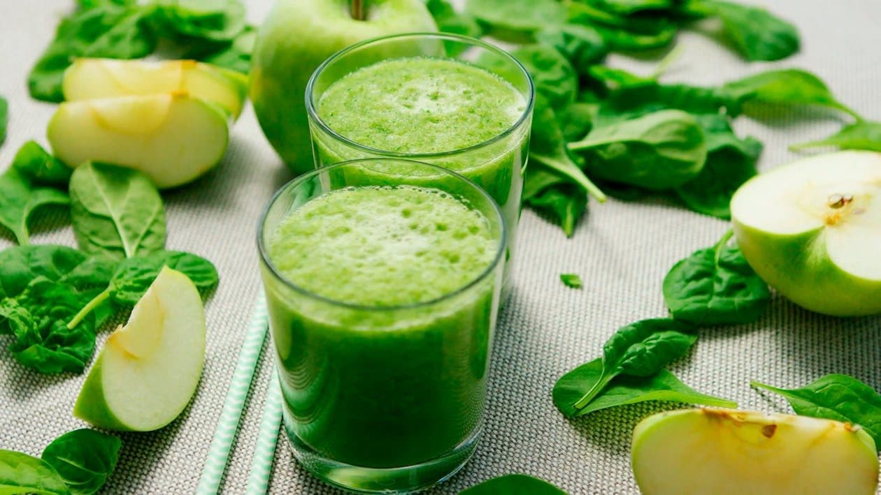 Fresh green smoothies surrounded by spinach and apple